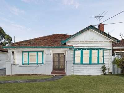 White single-story bungalow with teal window trim, a small porch stairway, and a bay window on the right; manicured front lawn.