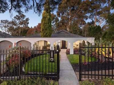 Front view of a single-story house with a white arched porch, black iron gate, and a paved walkway.