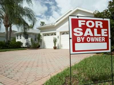 Residential house with a red-and-white 'For Sale by Owner' sign in the front yard.
