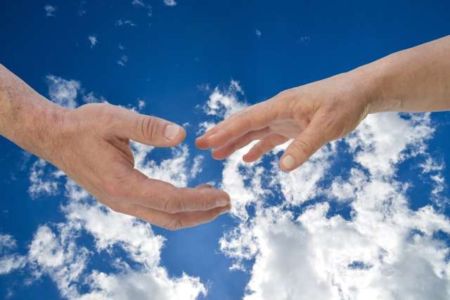 Two hands reaching toward each other against a bright blue sky with white clouds, about to connect.